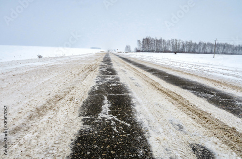 The road is covered with ice and covered with snow. The danger of black ice and poor visibility. Asphalt highway in the countryside, outside the city.
