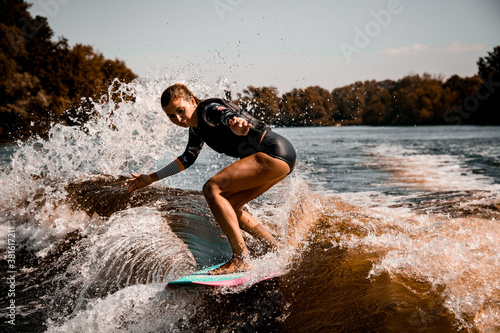 Beautiful woman stands with bent knees on surf style wakeboard and ride on wave