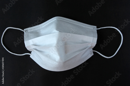 White protective medical face mask on a black background. Concept of protection during influenza, coronavirus pandemic.