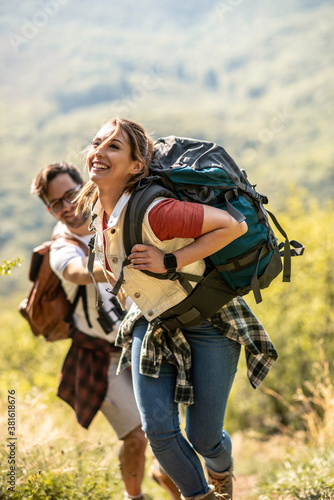 A young couple climbs a mountain, a beautiful day in nature, she smiles and carries a backpack for hiking