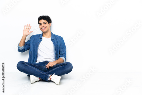 Venezuelan man sitting on the floor saluting with hand with happy expression © luismolinero