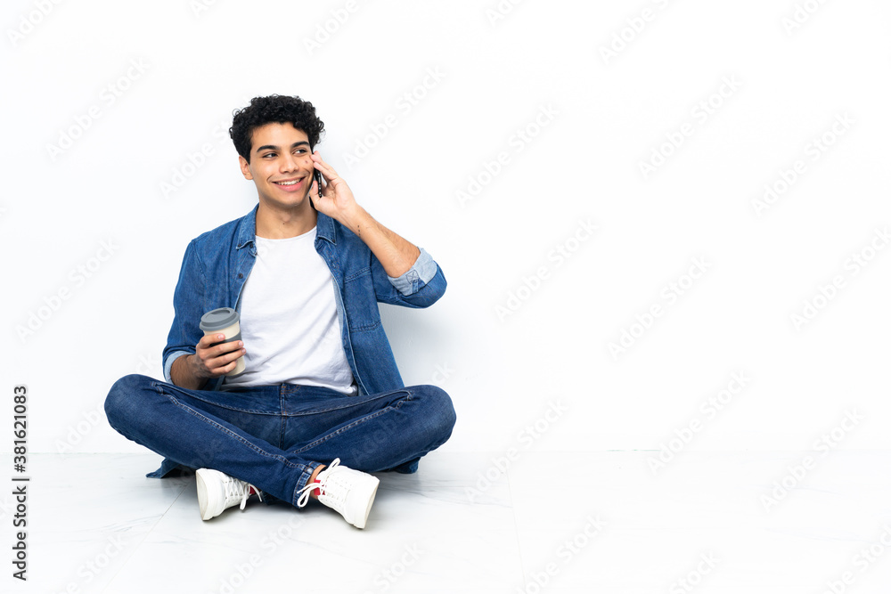 Venezuelan man sitting on the floor holding coffee to take away and a mobile Venezuelan man sitting on the floor holding coffee to take away and a mobile