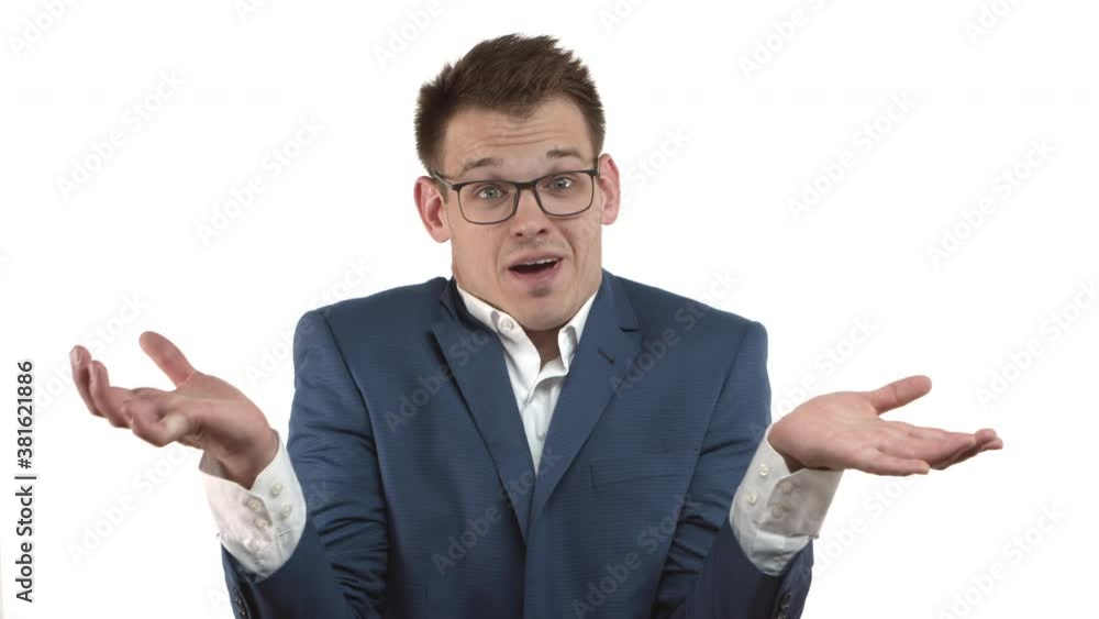 Handsome young businessman in blue suit and glasses looking clueless, shrugging and shaking head, dont know anything, standing over white background