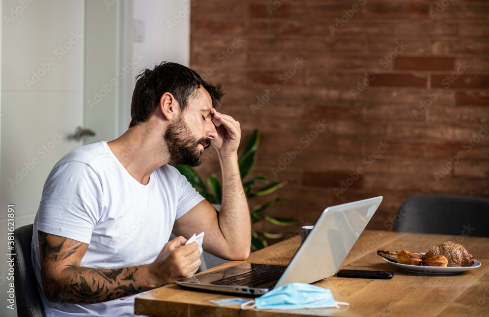 A young man is sitting alone in front of a laptop in the morning has symptoms of the virus, he will stay at home in quarantine A young man is sitting alone in front of a laptop in the morning has symptoms of the virus, he will stay at home in quarantine