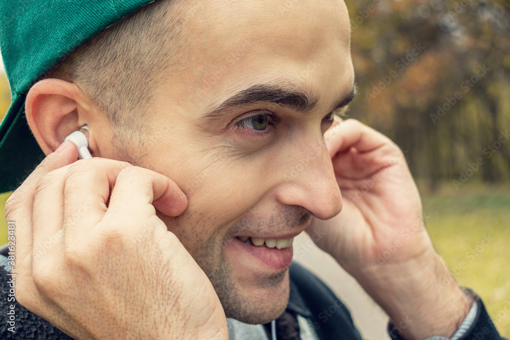Obraz premium Happy guy listens to music with headphones, man walking in the Park in spring, portrait, closeup