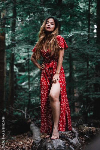 Beautiful Asian woman in red dress standing in a forest