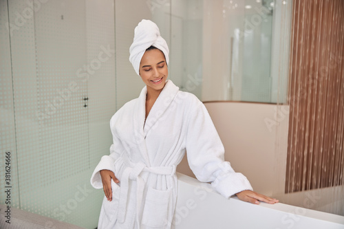 Cheerful young woman standing by bathtub in spa salon