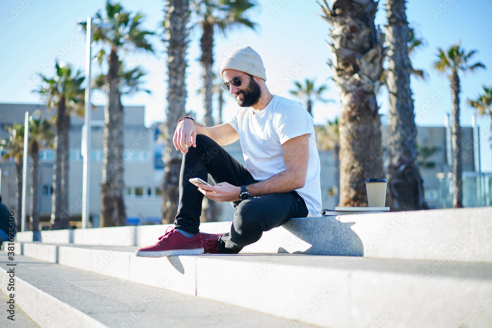 Happy young ethnic man messaging on smartphone while sitting on stairs in street Happy young ethnic man messaging on smartphone while sitting on stairs in street