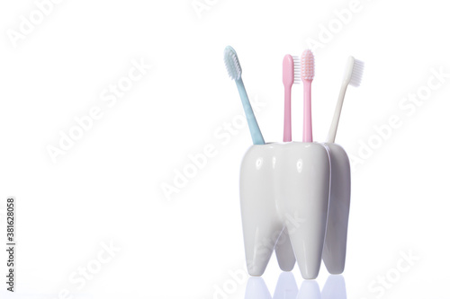 Four toothbrushes in ceramic tooth-shaped stand isolated on white background. Oral care routine, personal hygiene, healthy oral cavity, family bathroom equipment. Copy space, dental poster concept
