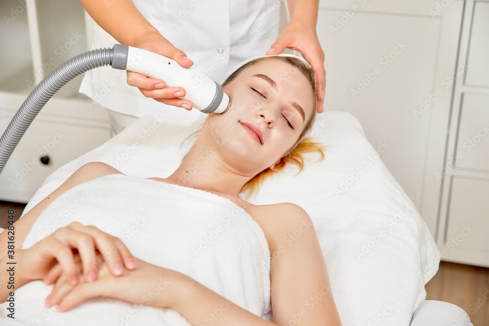 Obraz premium Close-up cosmetologist making ultrasound hardware cleaning of the face of her patient a beautiful young woman. Concept skin cleansing and restoration of elasticity