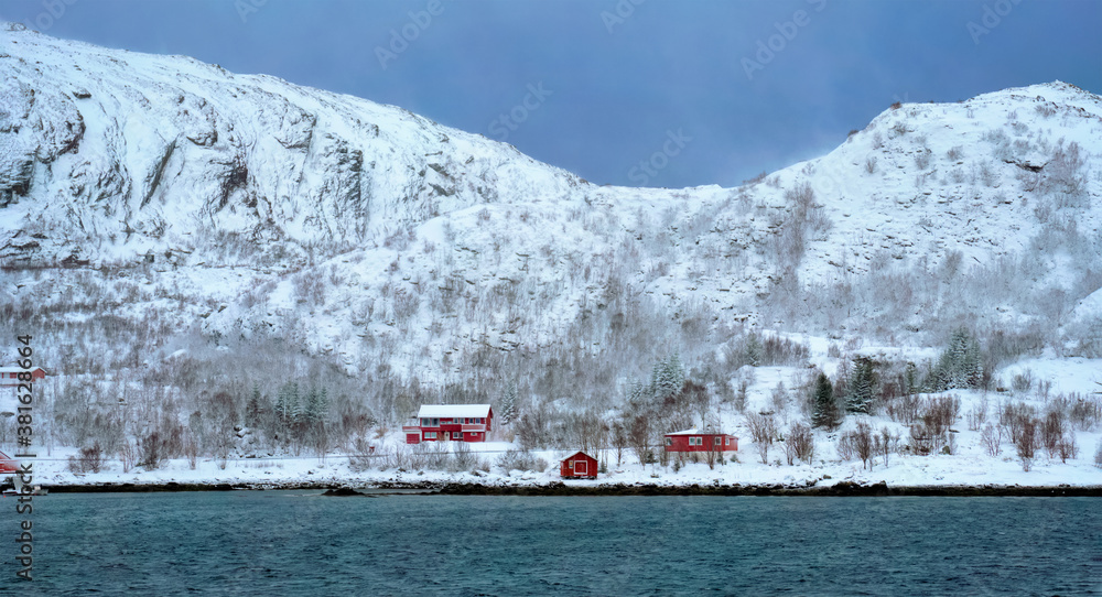 Panorama of traditional red rorbu houses on fjord shore in snow in winter. Lofoten islands, Norway
