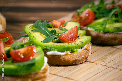 Avocado mash and fresh sliced tomatoes on grilled toast bread on brown wooden background. Trendy and healthy breakfast.