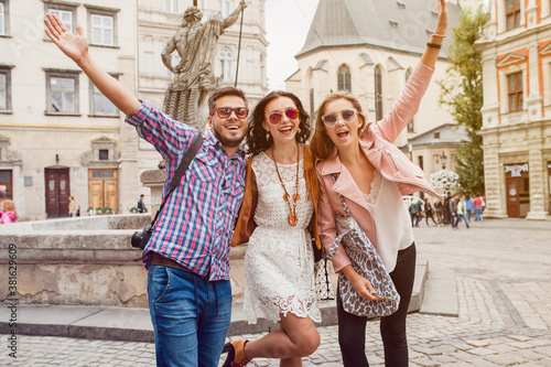 young hipster company of friends traveling  vintage style  europe vacation  sunglasses  old city center  happy positive mood  smiling  embracing  pointing finger  looking forward