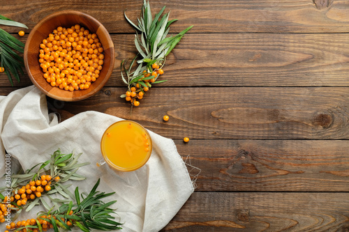 Sea buckthorn juice and sea buckthorn berries in bowl, plant branches on wooden table. Flat lay composition, top view.