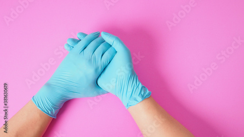 Two hand wear blue latex gloves and hold hands on PINK background.