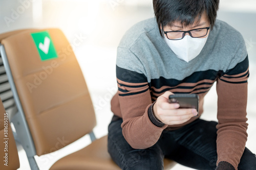 Asian man tourist wearing face mask using smartphone in airport terminal. Coronavirus (COVID-19) pandemic prevention when travel abroad. Health awareness and social distancing
