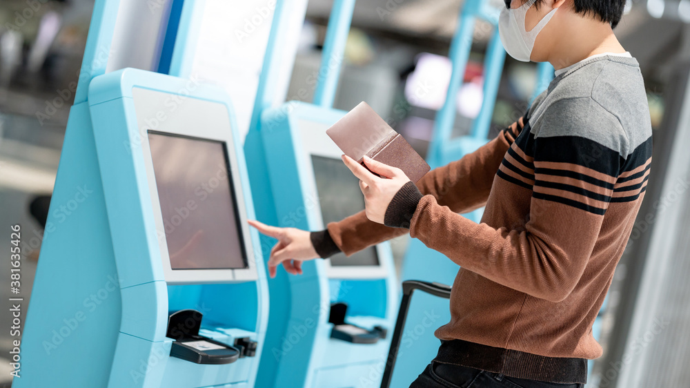 Asian man tourist wearing face mask using self check-in kiosk in airport terminal. Coronavirus (COVID-19) pandemic prevention when travel abroad. Health awareness and social distancing concept Asian man tourist wearing face mask using self check-in kiosk in airport terminal. Coronavirus (COVID-19) pandemic prevention when travel abroad. Health awareness and social distancing concept