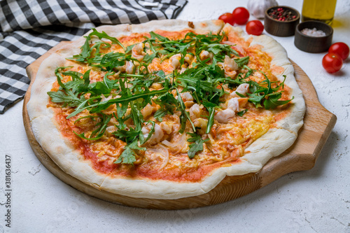 Pizza with arugula and shrimps on white concrete table