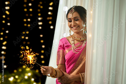 Woman looking at the sparkler in her hand  with a smile on the occasion of Diwali	 photo