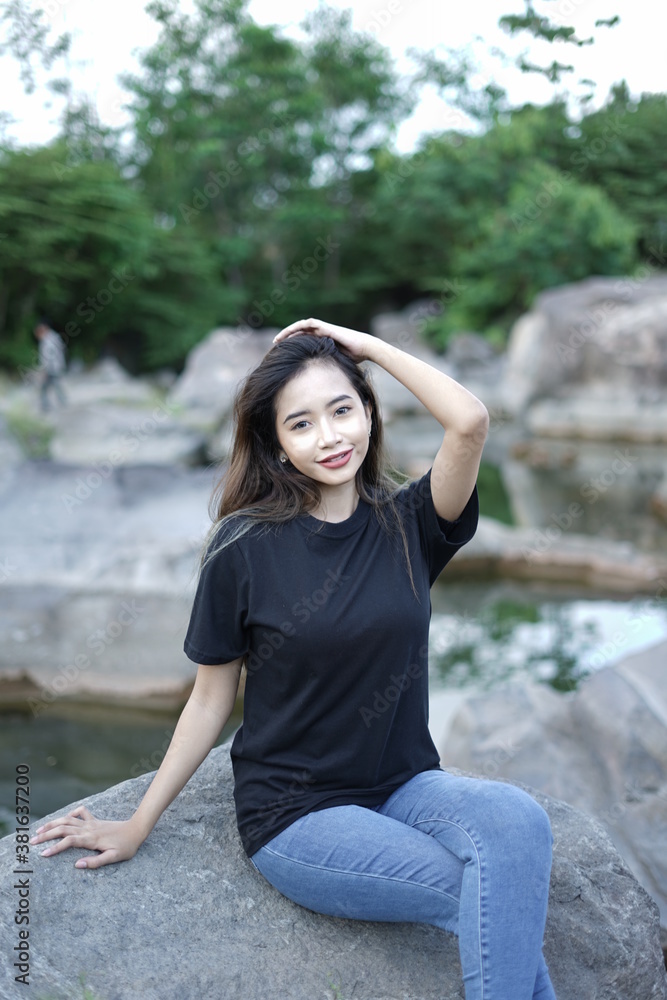 Stylish blonde girl wearing a black shirt with views of natural rocks, lake water and clear sky. female t-shirt models for mockups and templates. Stylish blonde girl wearing a black shirt with views of natural rocks, lake water and clear sky. female t-shirt models for mockups and templates.