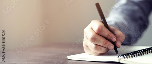 close up hand young man are sitting using pen writing Record Lecture note pad into the book on the table wood.