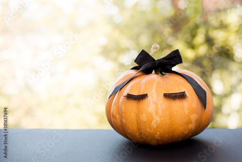 Halloween pumpkin with make up eyelashes and black bow. Holiday season concept.