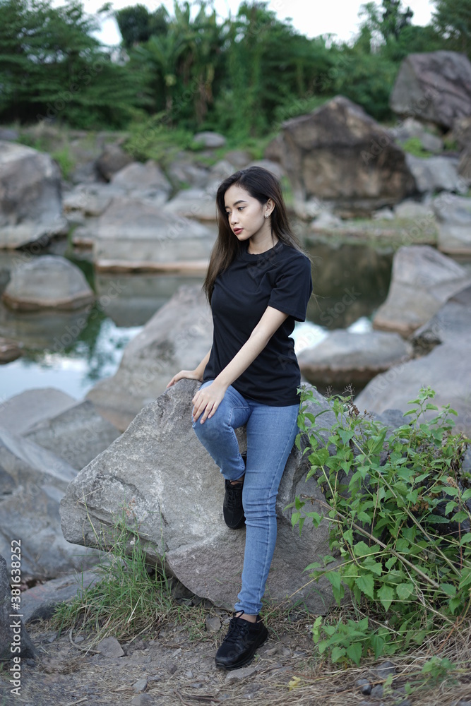 Stylish blonde girl wearing a black shirt with views of natural rocks, lake water and clear sky. female t-shirt models for mockups and templates.