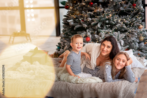 Happy cheerful family near Christmas tree. Mother and kids wearing pajama having fun near tree in the morning. © len44ik