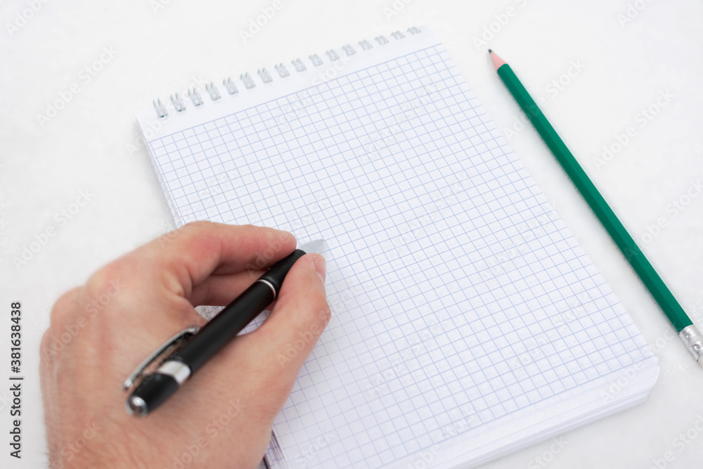 Person is left handed writes something in a notebook, makes notes, notebook, pencil, men's hand, closeup, top view, copy space Person is left handed writes something in a notebook, makes notes, notebook, pencil, men's hand, closeup, top view, copy space