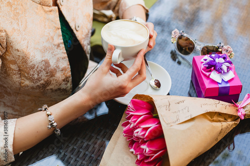 young stylish woman, sitting in cafe, holding drinking cup cappuccino, smiling, enjoying warm, presents, tulips, happy birthday party, city street, europe vacation, detail, close up