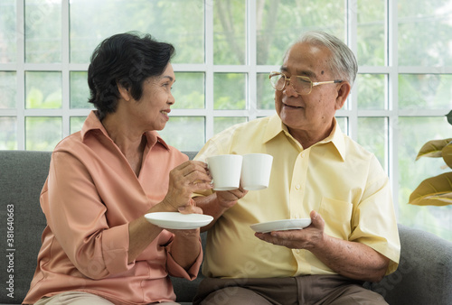 Senior Asian elderly couple in home casual outfit with happy smiling emotion sitting in living room drinking coffee or tea for breakfast together