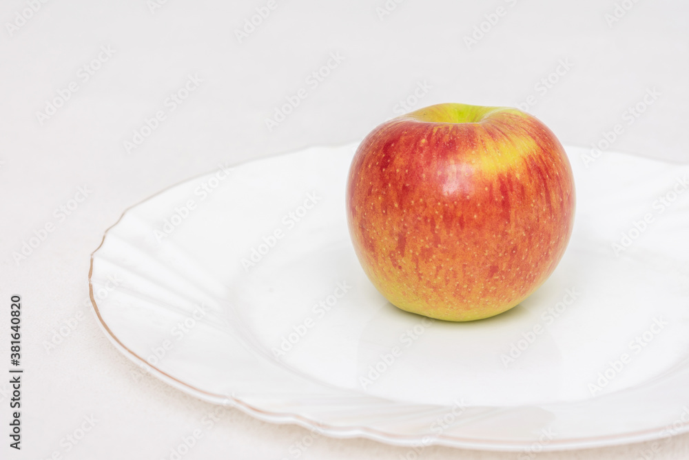 A ripe red Apple on a white plate, closeup, side view A ripe red Apple on a white plate, closeup, side view