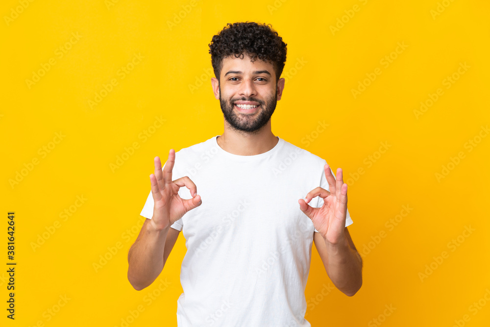 Young Moroccan man isolated on yellow background showing ok sign with two hands Young Moroccan man isolated on yellow background showing ok sign with two hands