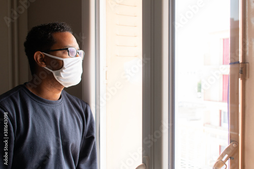 Coronavirus Sick man from corona virus looking out the window and wearing mask for protection and recovery from illness at home. Quarantine. Isolated patient to prevent infection. Pandemic. House. 