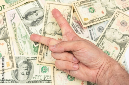 Man shows sign peace with fingers, dollar bills in the background, male hand, close-up