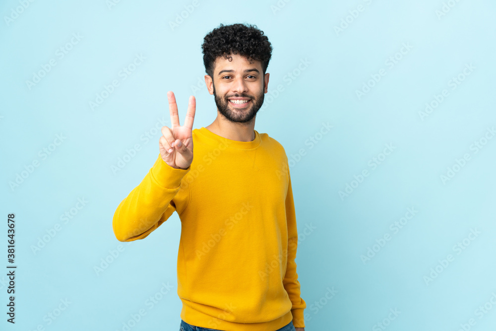 Young Moroccan man isolated on blue background smiling and showing victory sign Young Moroccan man isolated on blue background smiling and showing victory sign