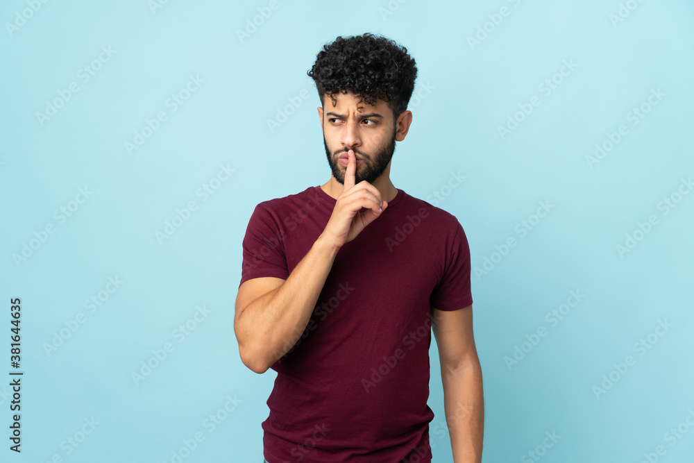 Young Moroccan man isolated on blue background showing a sign of silence gesture putting finger in mouth Young Moroccan man isolated on blue background showing a sign of silence gesture putting finger in mouth