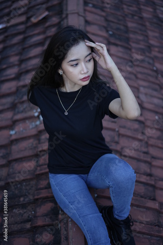 The blonde girl sits on the roof tile while stylish wearing a black t-shirt. female t-shirt models for mockups and templates. © AndhikaRaya