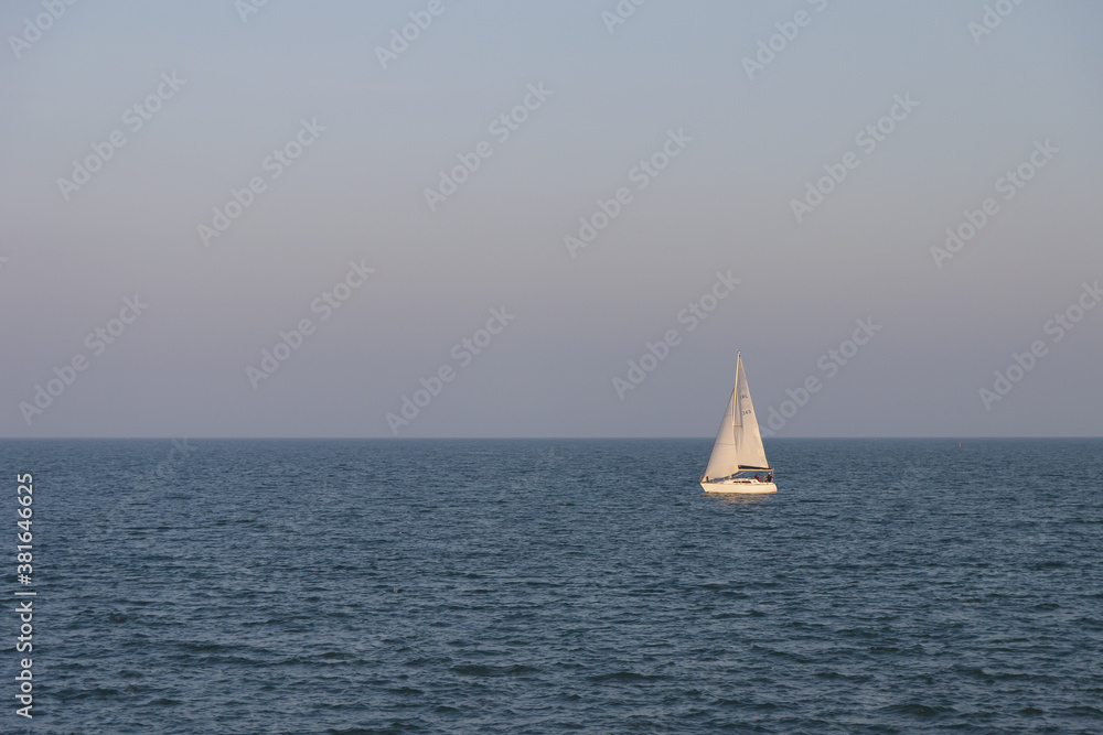 Single boat sails across the vastness of the sea