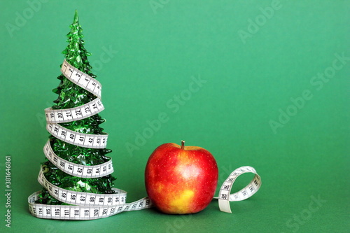 A centimeter-long ribbon is wrapped around a small green toy Christmas tree next to an Apple. The concept of healthy and healthy food during the Christmas holidays. The concept of weight loss .