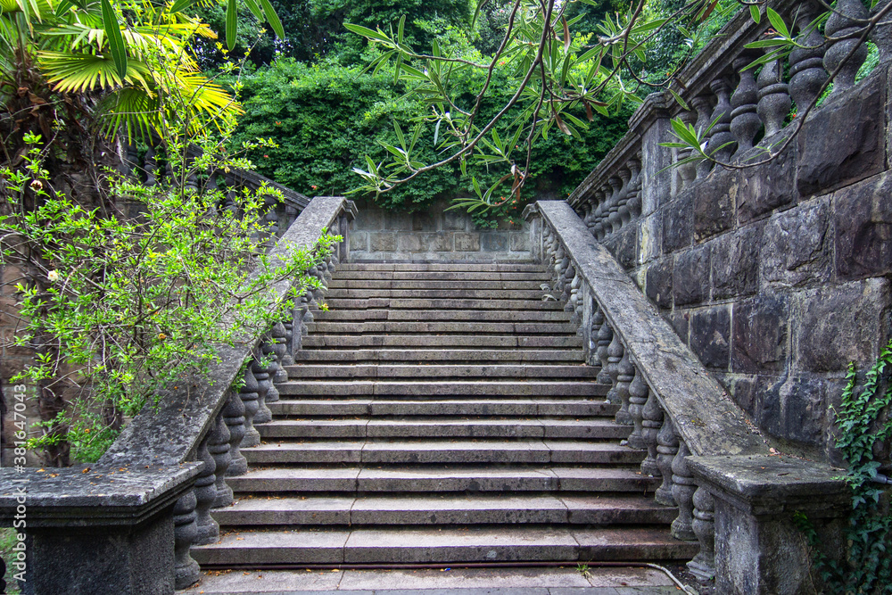 Ancient staircase are grey stone with stone balusters on a background of green vegetation Ancient staircase are grey stone with stone balusters on a background of green vegetation