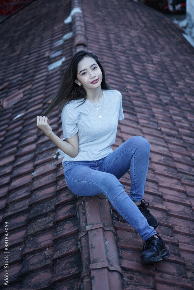 The blonde girl sits on the roof tile while stylishly wearing a gray shirt. female t-shirt models for mockups and templates. The blonde girl sits on the roof tile while stylishly wearing a gray shirt. female t-shirt models for mockups and templates.
