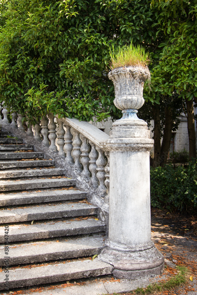 Stone pot as a decorative element of an ancient staircase with stone balusters on a background of green vegetation