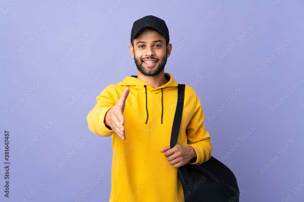 Young sport Moroccan man with sport bag isolated on purple background shaking hands for closing a good deal