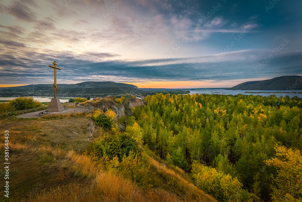 Beautiful landscape with a cross on a hill, surrounded on all sides by forest, river and mountains on the horizon with dawn sky and clouds. Beautiful landscape with a cross on a hill, surrounded on all sides by forest, river and mountains on the horizon with dawn sky and clouds.
