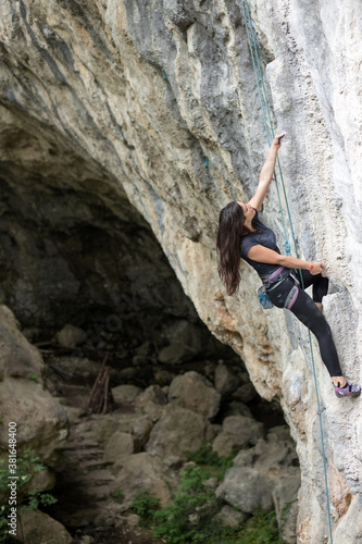 Determined fit young Caucasian woman climbing steep overhanging tufa line on a top-rope in a cave, trying to push her limits
