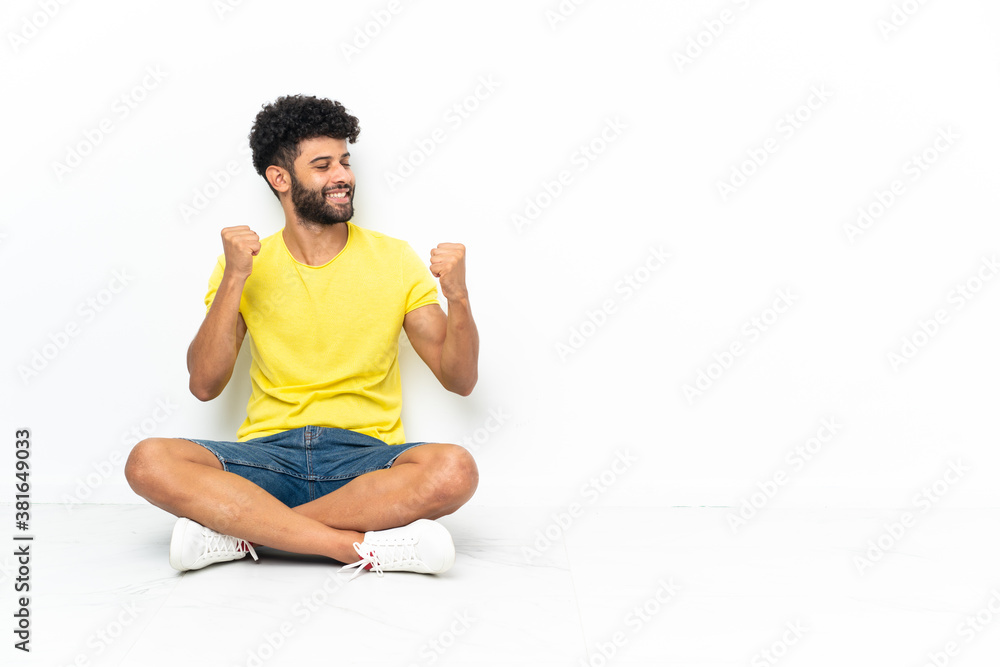 Fototapeta premium Young Moroccan handsome man sitting on the floor over isolated background celebrating a victory