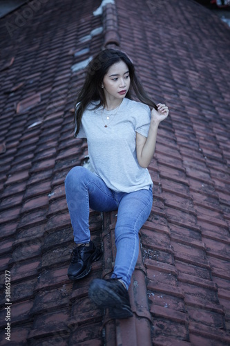 The blonde girl sits on the roof tile while stylishly wearing a gray shirt. female t-shirt models for mockups and templates. © AndhikaRaya
