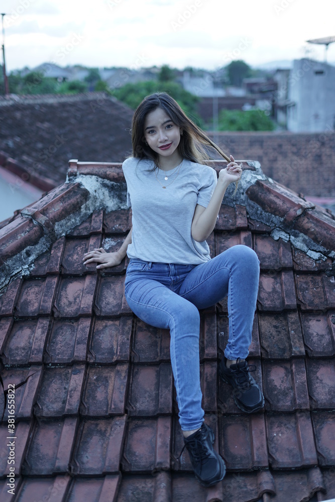 The blonde girl is sitting and stylish wearing a white T-shirt on the roof of the house with a view of the clear sky. female t-shirt models for mockups and templates.