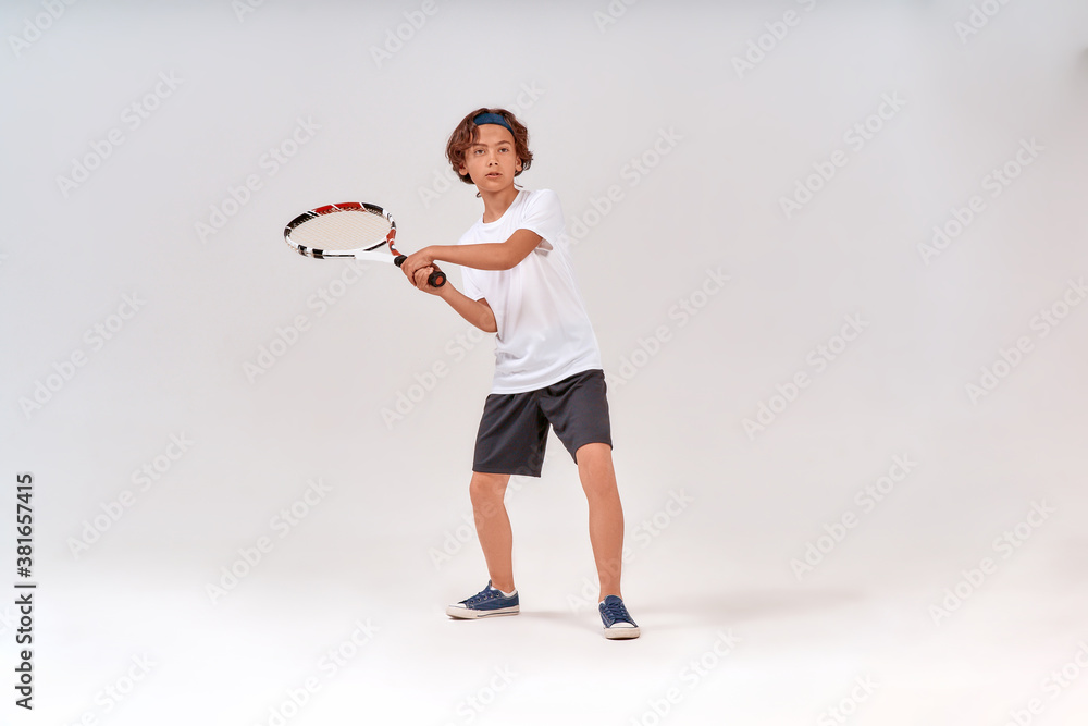 Playing tennis. Full-length shot of a teenage boy holding tennis racket and looking away isolated over grey background Playing tennis. Full-length shot of a teenage boy holding tennis racket and looking away isolated over grey background